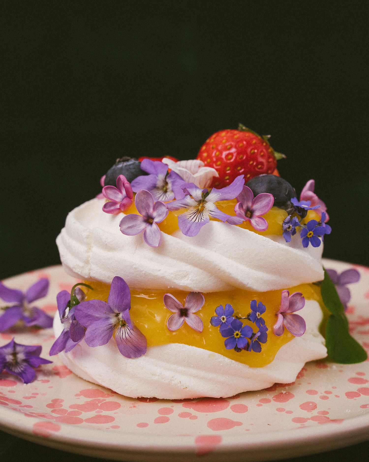Nærbilde av mini-pavlova med sitronsmør, spiselige blomster og vekster og jordbær.