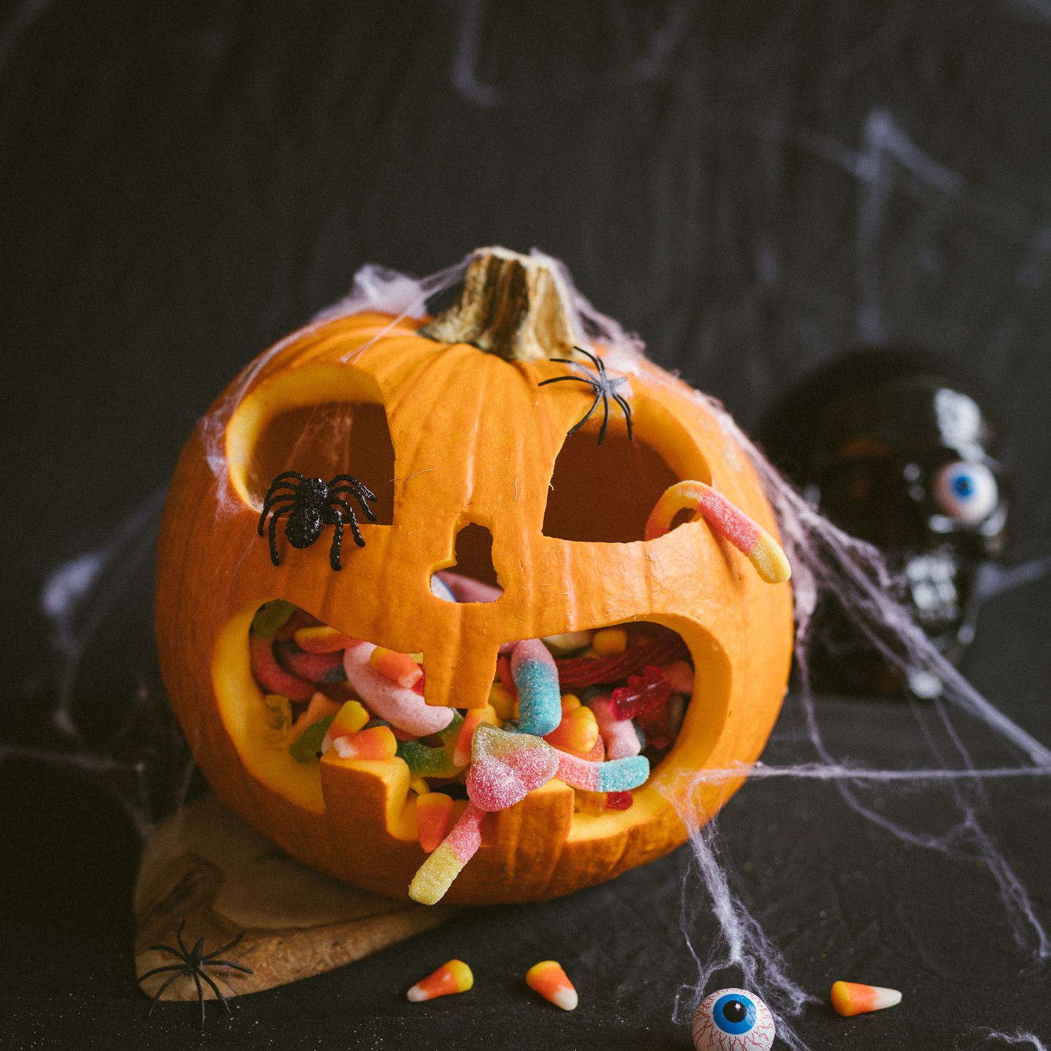 Et stort Halloween gresskar fylt med Candy King smågodt, spindelvev og svart hodeskalle i bakgrunnen.