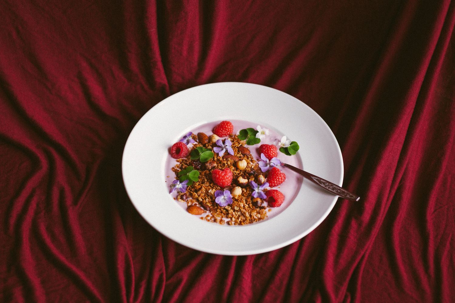 Hjemmelaget granola med yoghurt, bringebær og spiselige blomster.