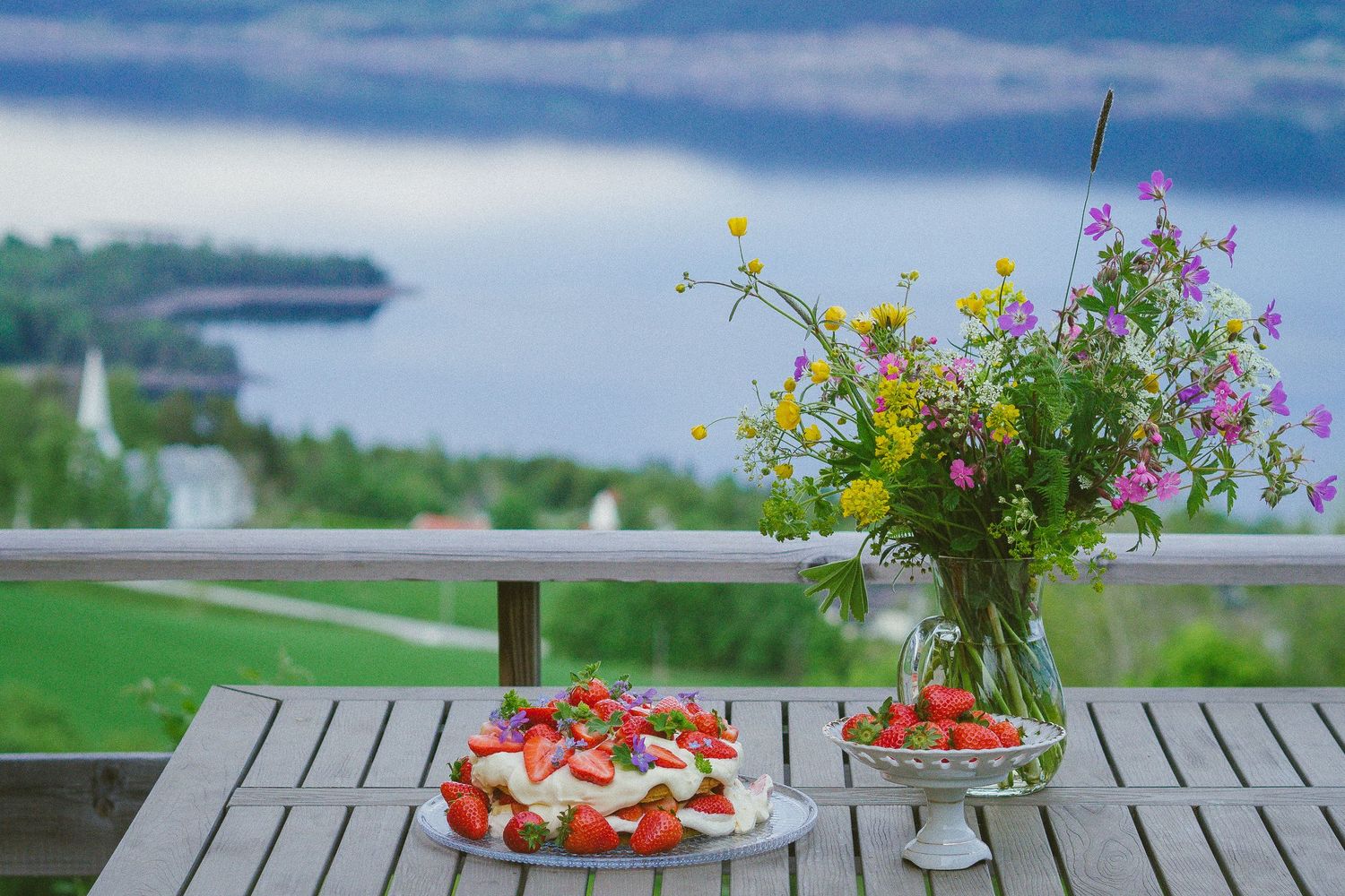 Sommerlig jordbærkake med markblomster og fjordutsikt.