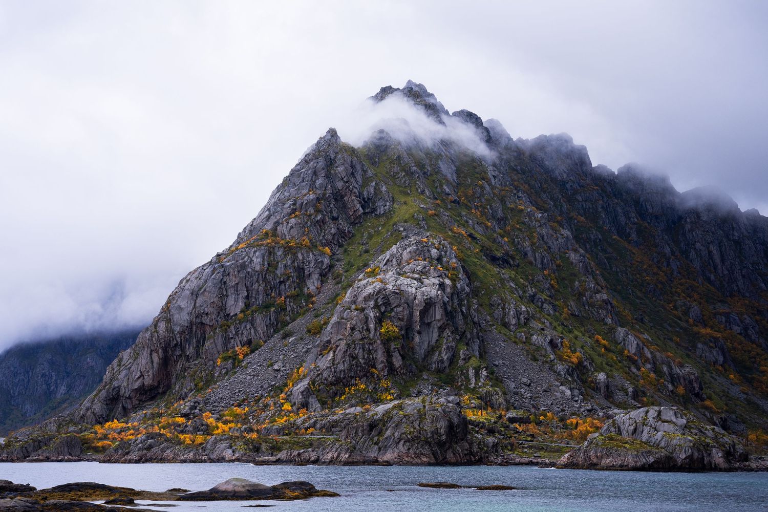 Dramatic coastal mountain range with low-hanging clouds and rugged cliffs.