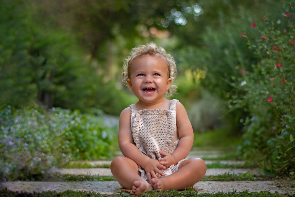 a toddler laughing to the camera in the beautiful Jerusalem Estates garden in Jerusalem, Israel.