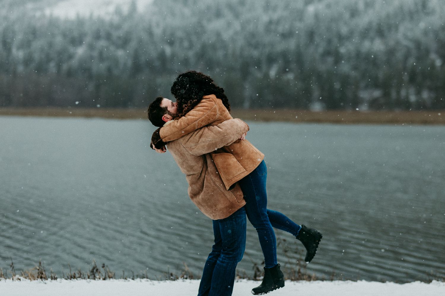 Man lifting his wife in the air romantically by a wintry lake