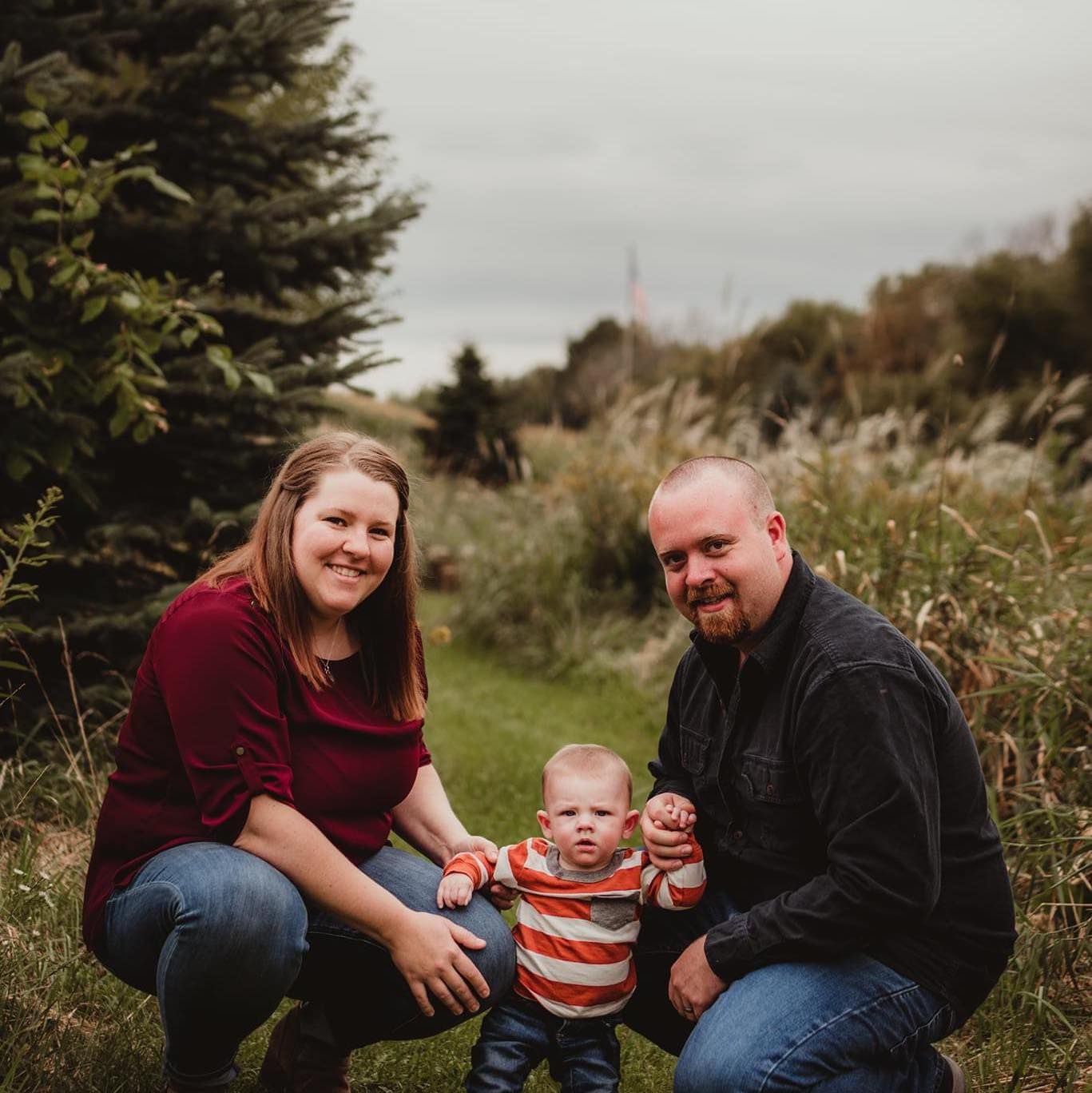 Family sitting together outdoors on grass with evergreen trees in the background.