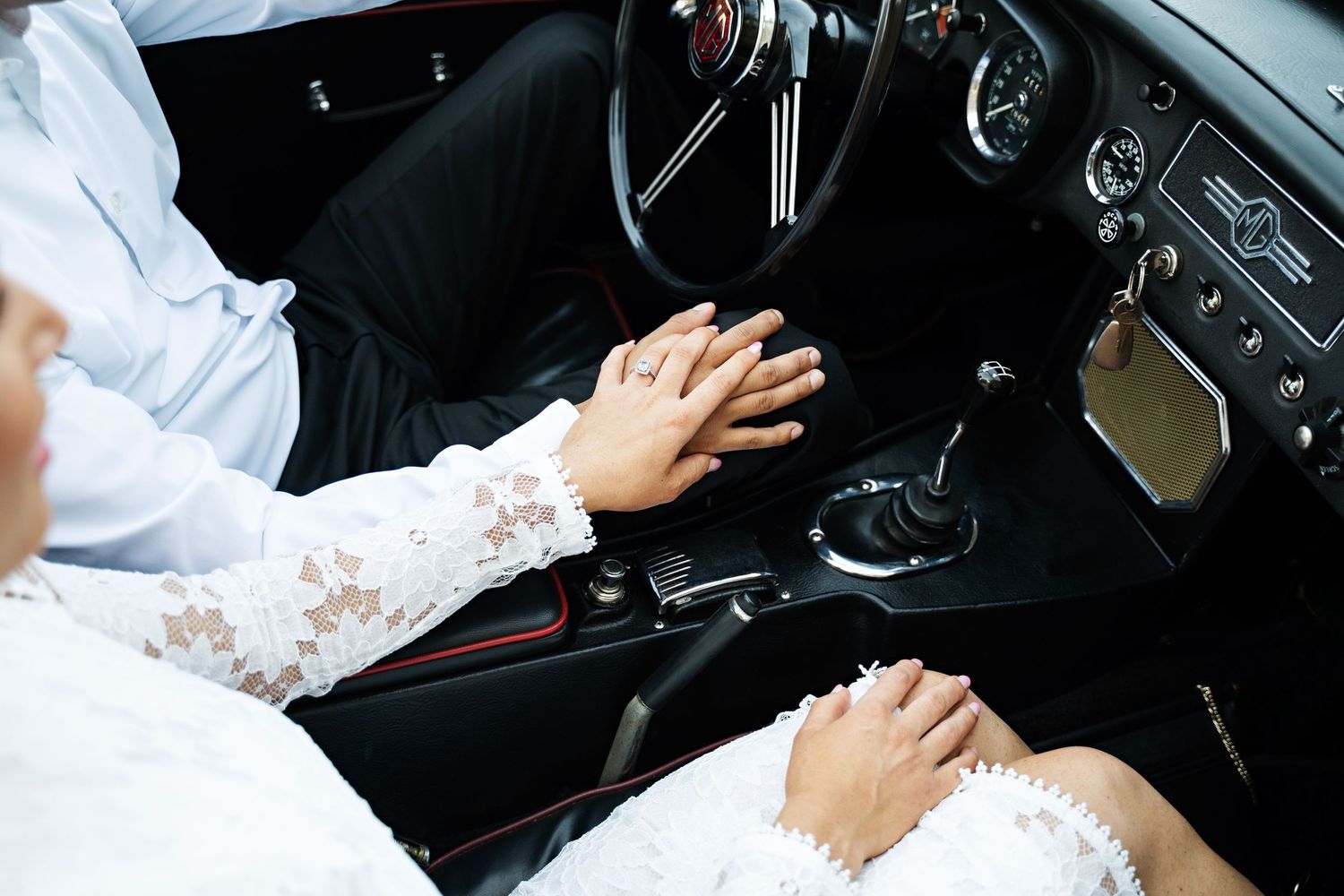 Newlywed couple sitting in a car with white wedding dress details visible.