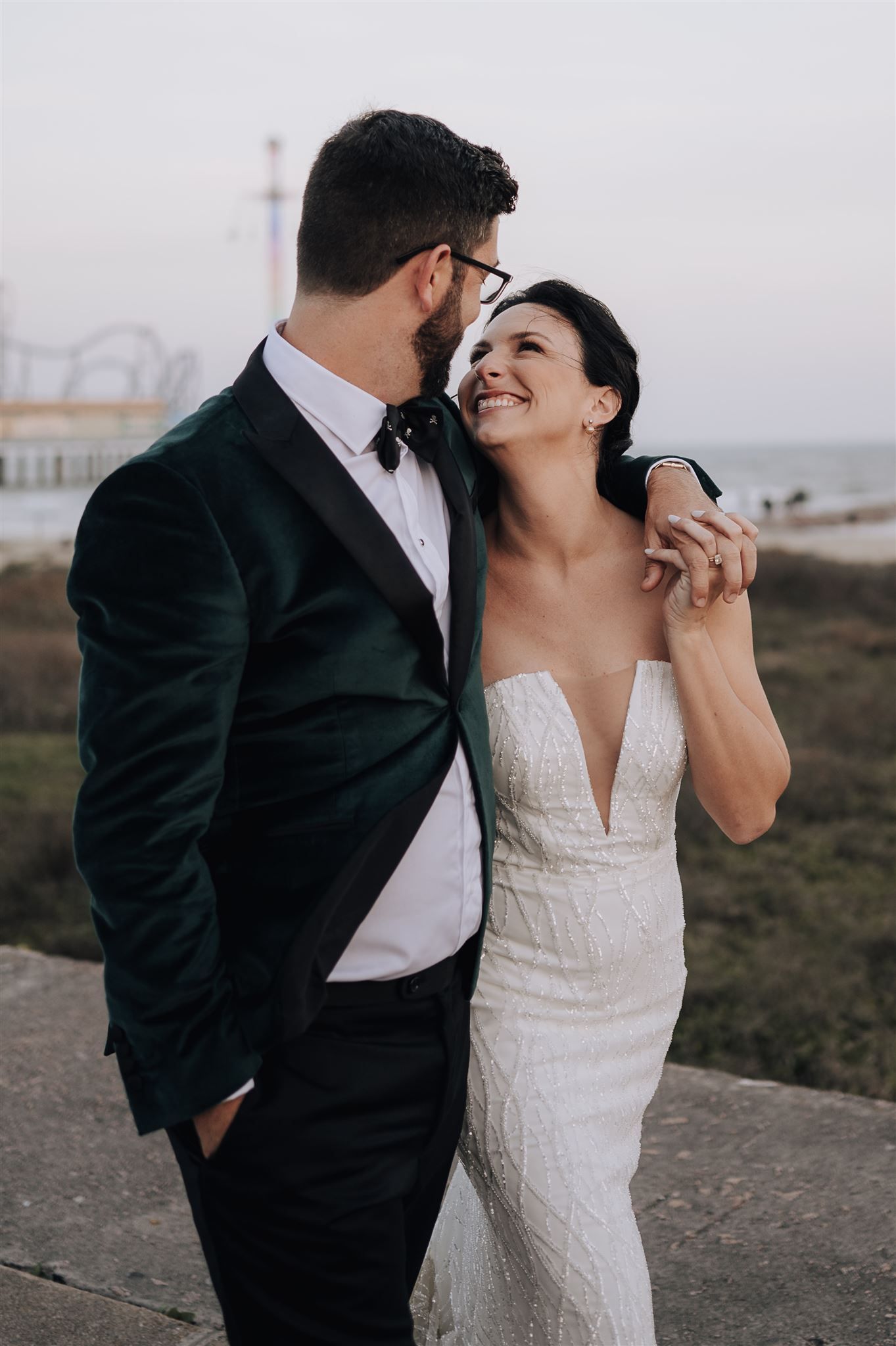 Wedding couple shares intimate moment with pier and coastline in background.