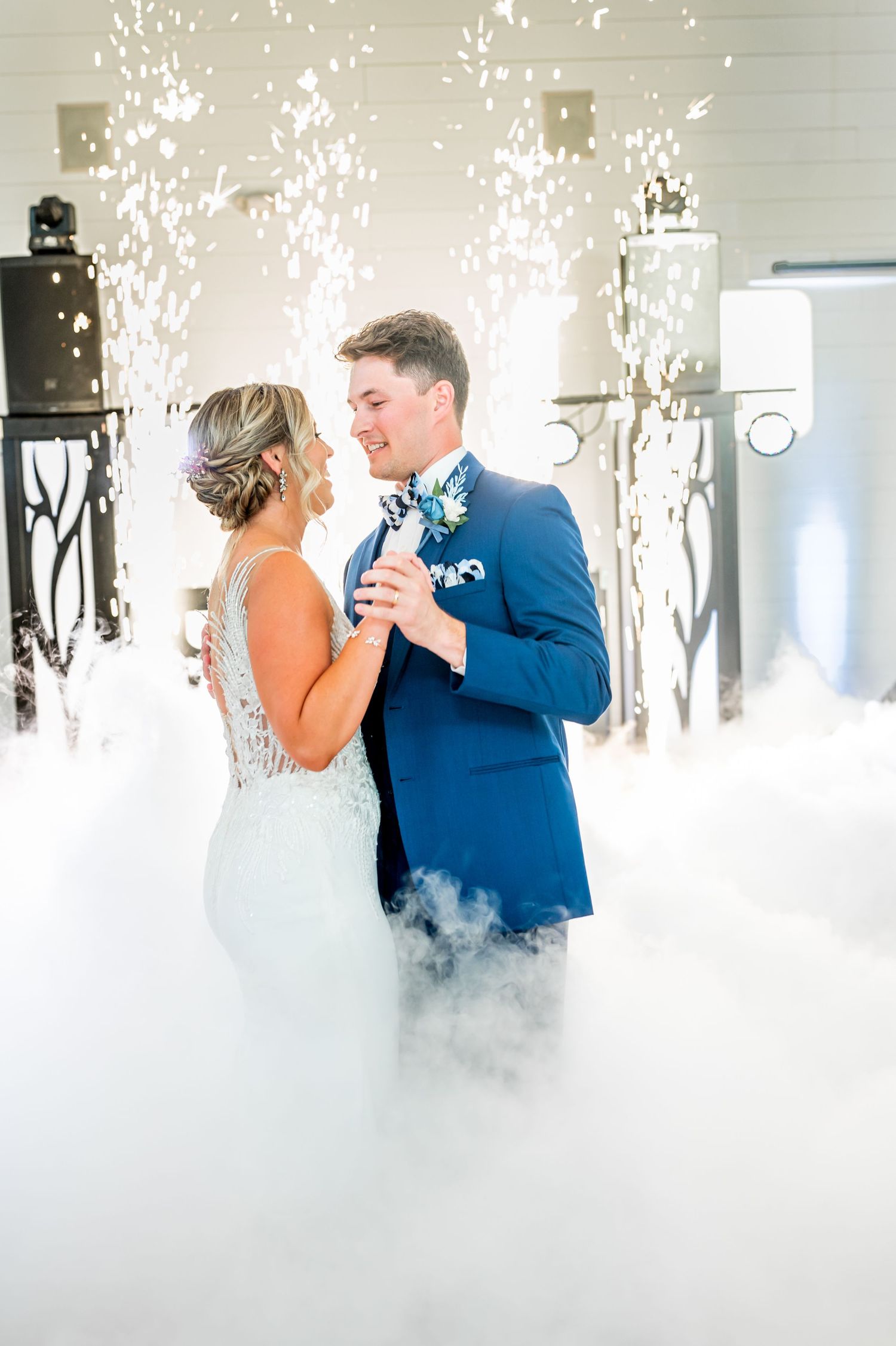 Newlyweds share their first dance surrounded by sparklers and fog effects creating a magical atmosphere.