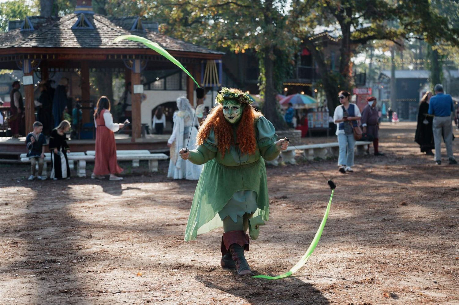 A performer in green costume twirling ribbons at a renaissance festival.