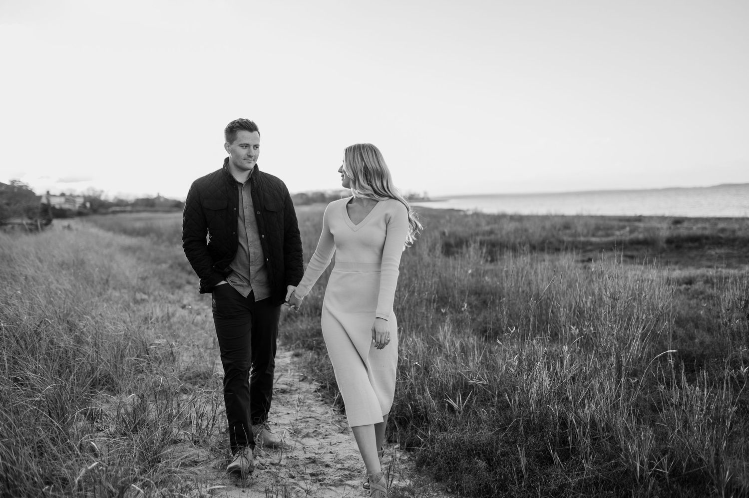Black and white photo of couple walking together through coastal grassland.