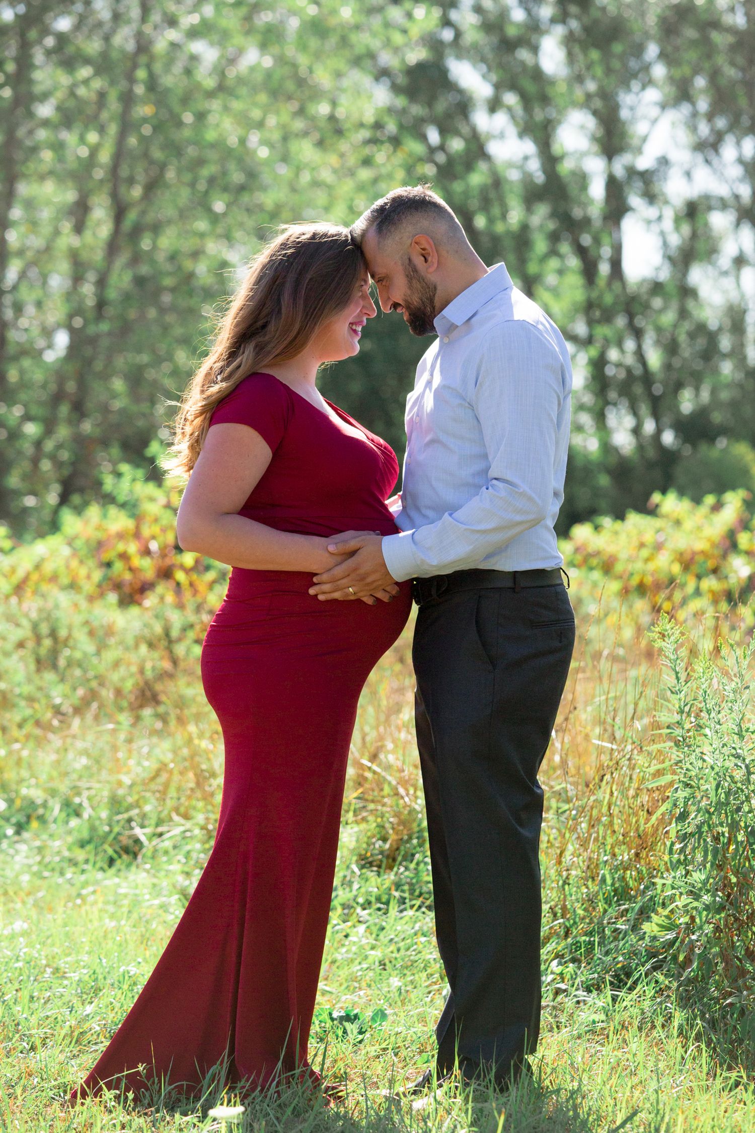 A romantic maternity photo of a couple embracing in a sunlit meadow with wildflowers.