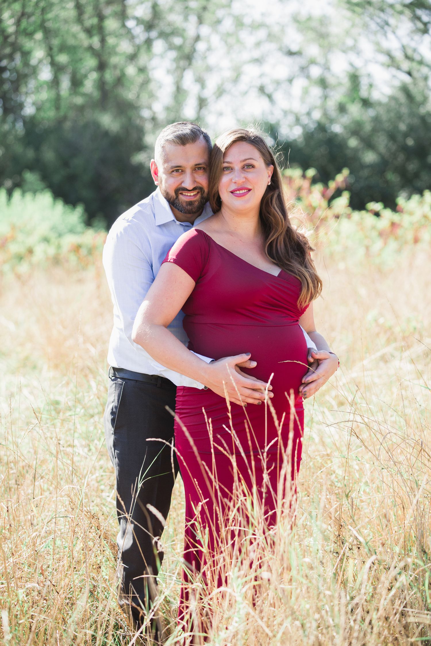Couple shares tender moment during maternity photoshoot in tall grass outdoors.