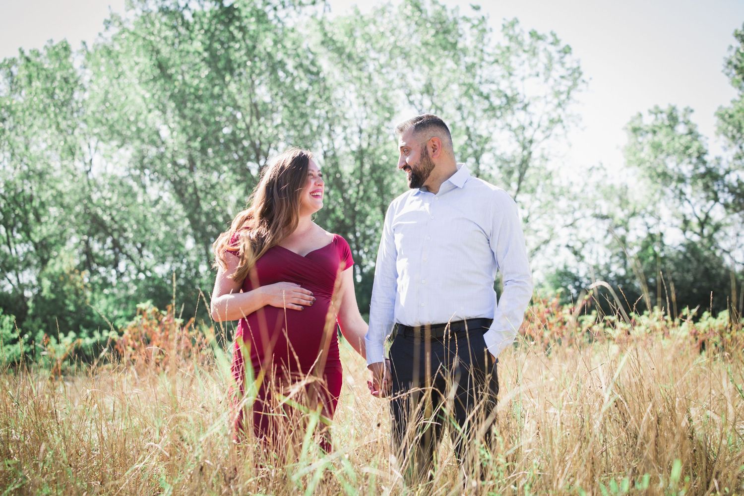 Couple walking together through golden grass field during sunset maternity photo session.