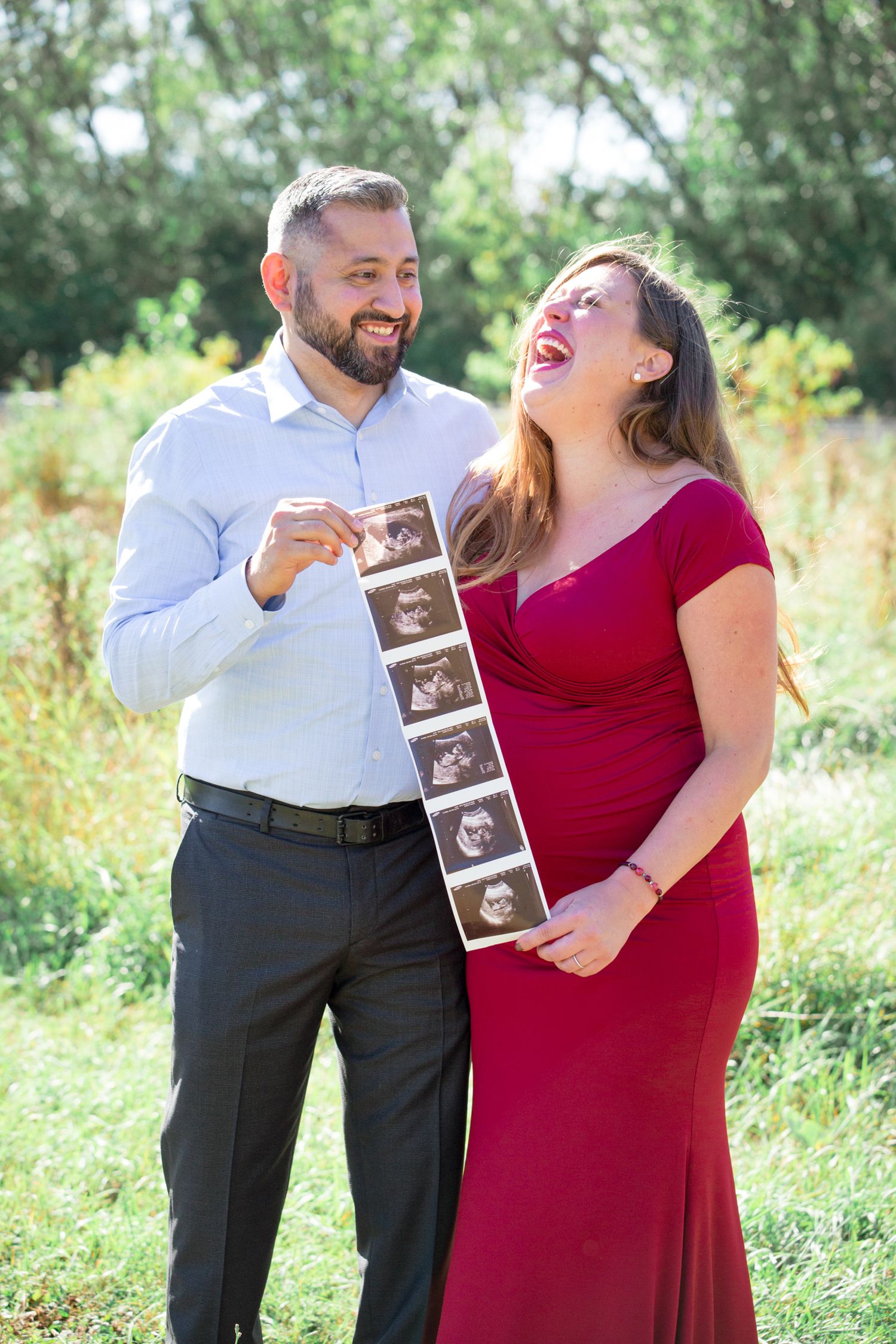 Joyful couple holding ultrasound photos during outdoor maternity photoshoot.