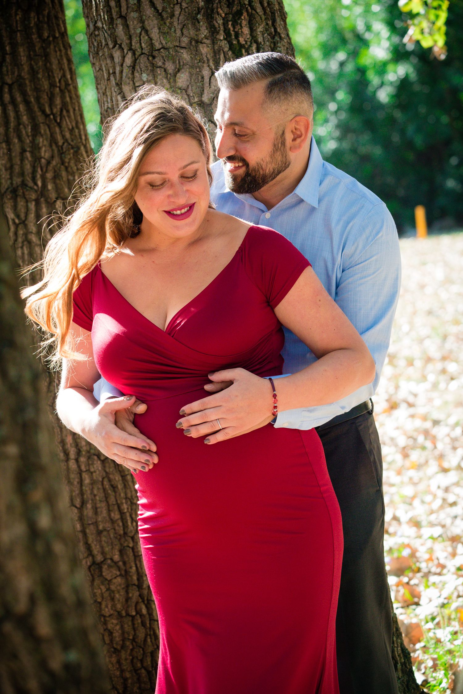 A romantic outdoor maternity photo featuring a couple embracing by a large tree.