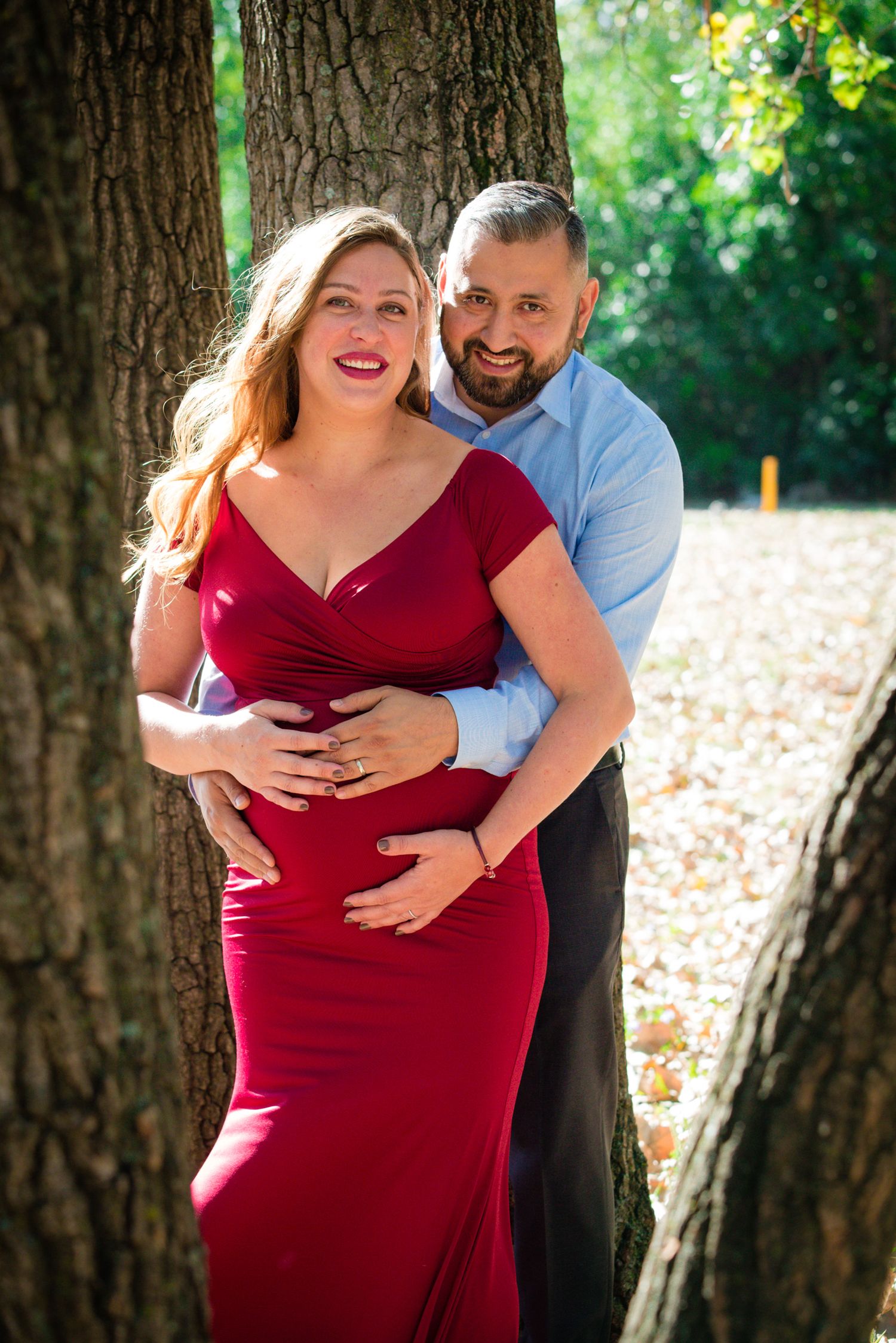 A joyful outdoor portrait showcasing an expecting couple against a natural woodland backdrop.