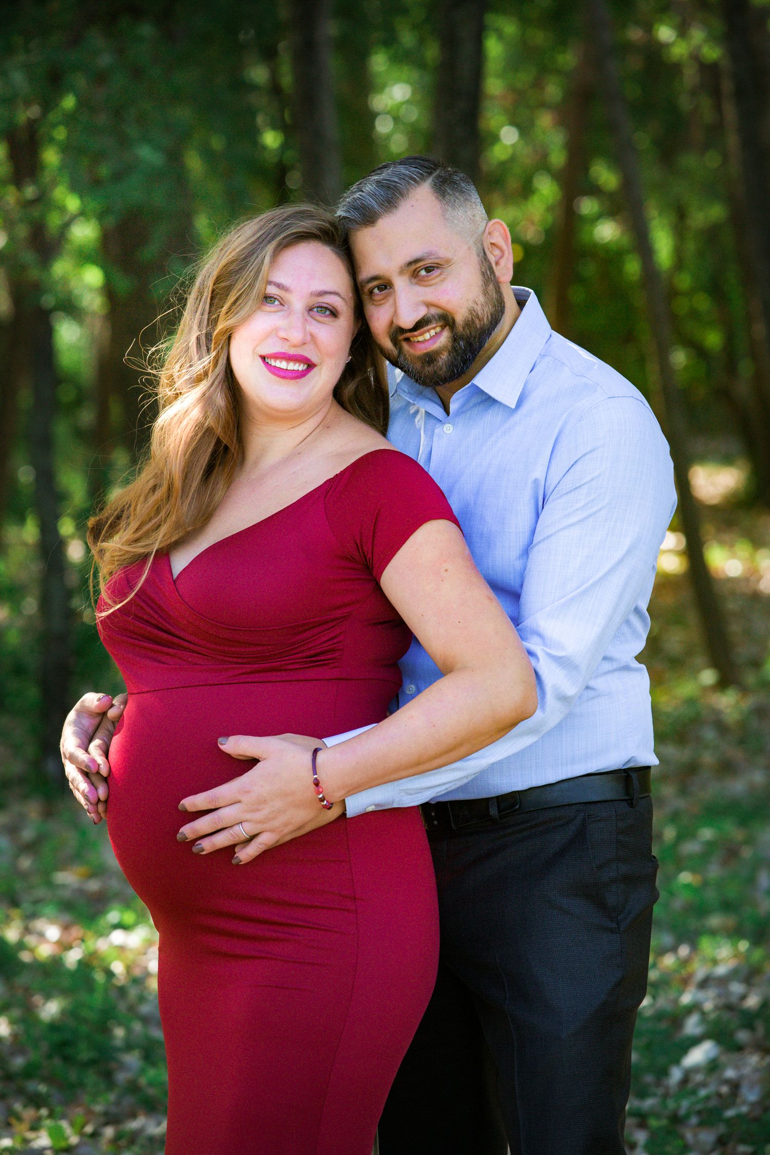 An intimate maternity portrait of a couple sharing a smile in a forest setting.