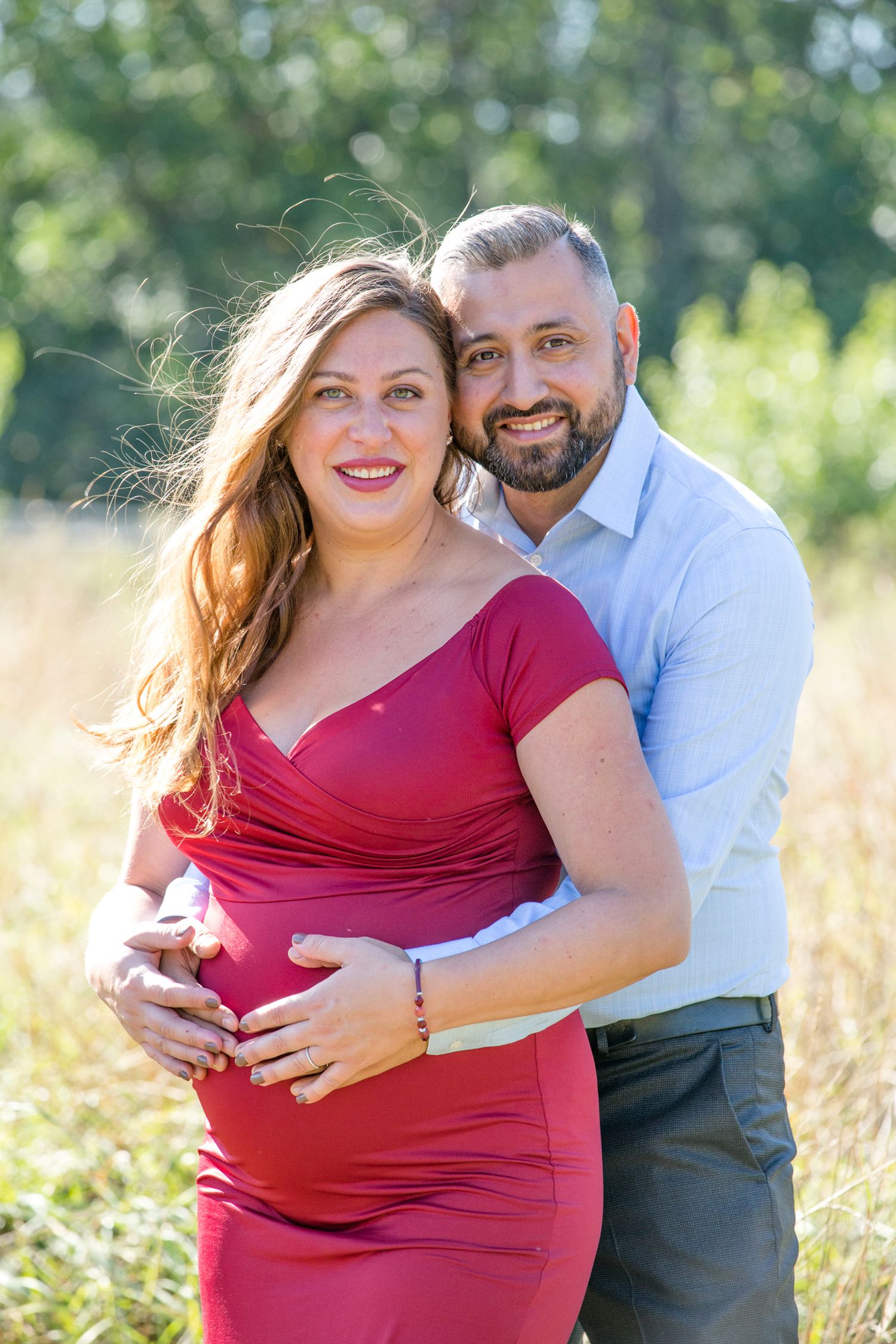 A sunlit maternity portrait captures a tender moment between a couple in a meadow.