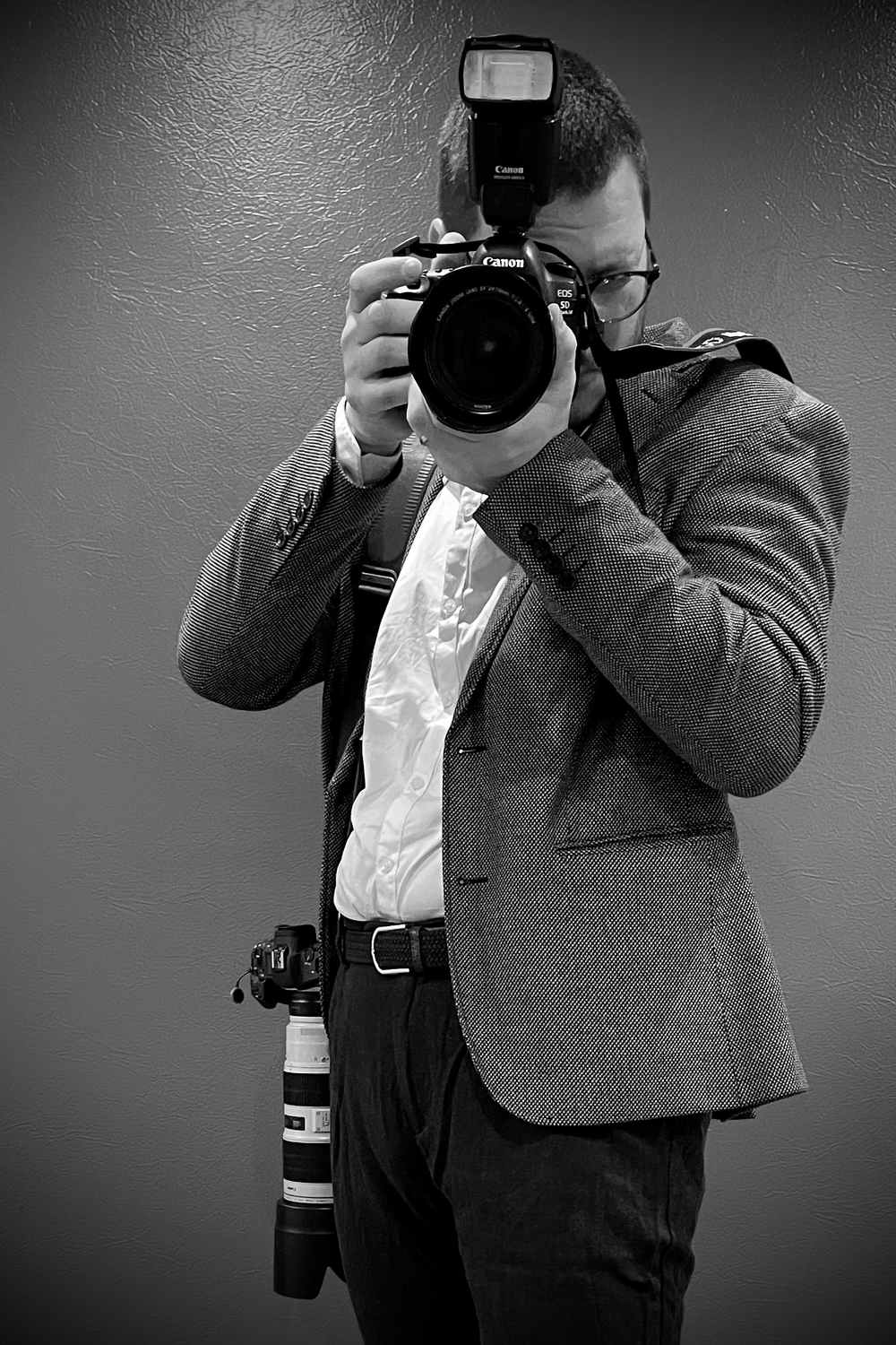 Professional photographer holding a DSLR camera with flash in a studio setting.
