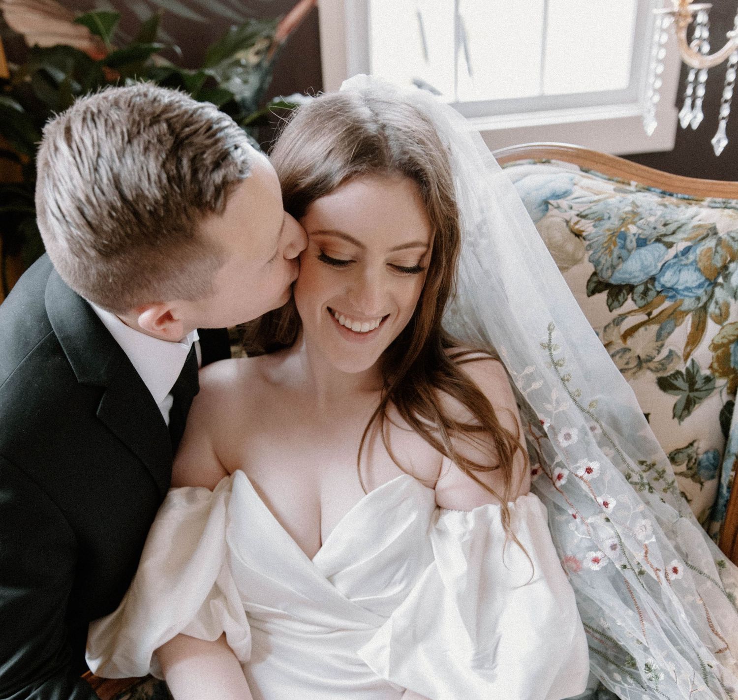 Intimate wedding portrait of couple sharing romantic moment on floral couch.