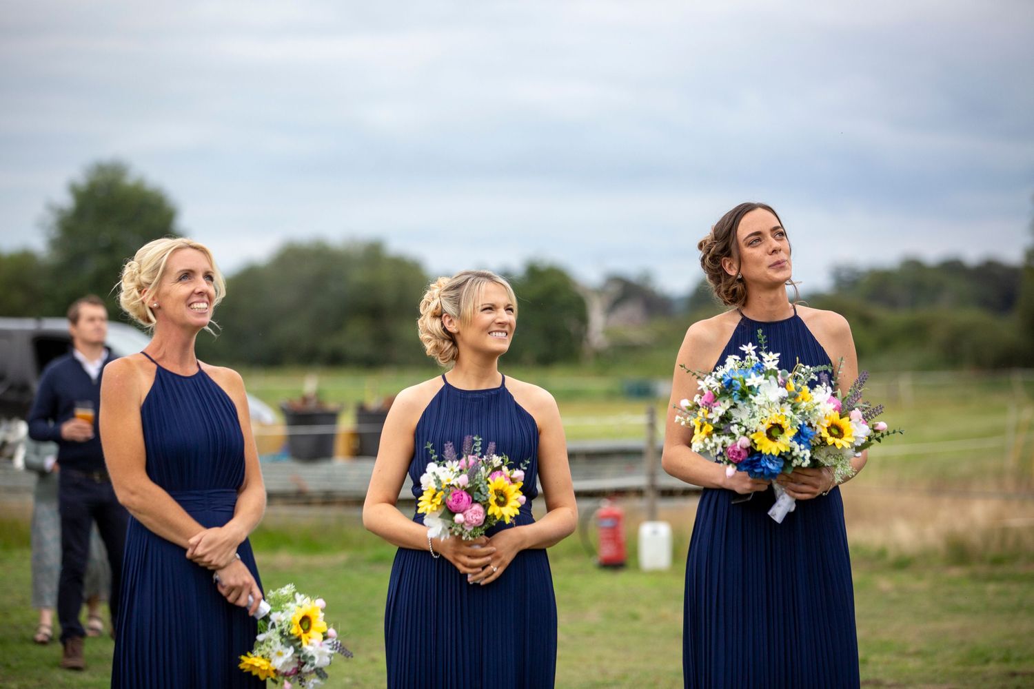 Bridesmaids in navy blue dresses holding colorful bouquets outdoors.