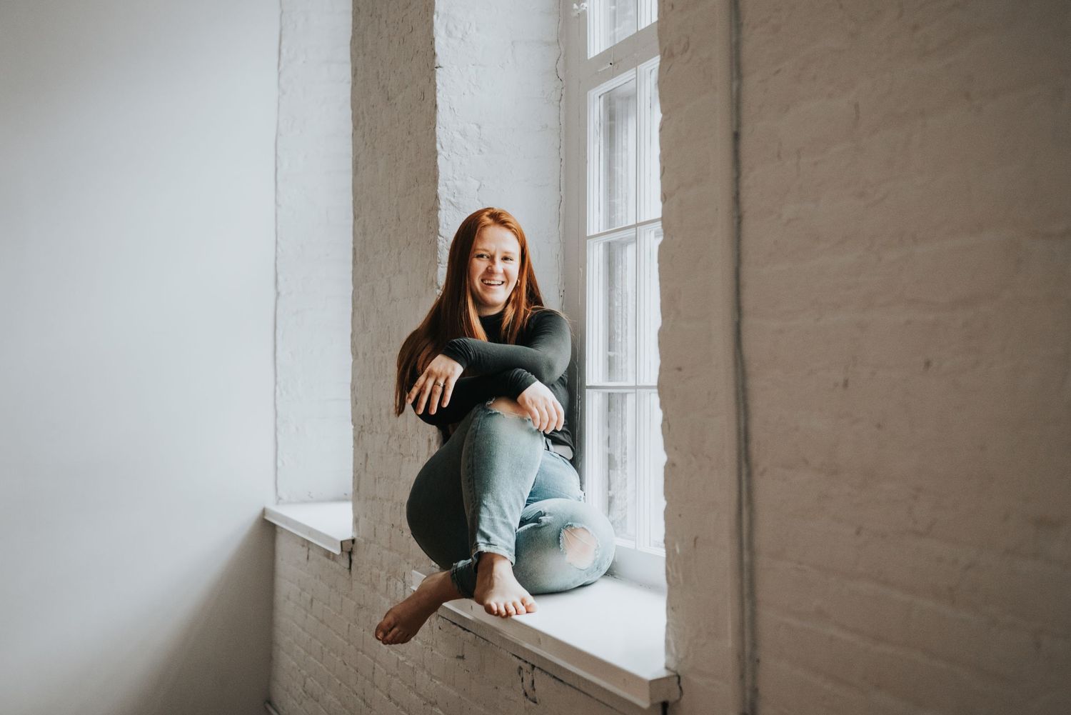 Portrait of a person sitting comfortably in a window sill with natural light.