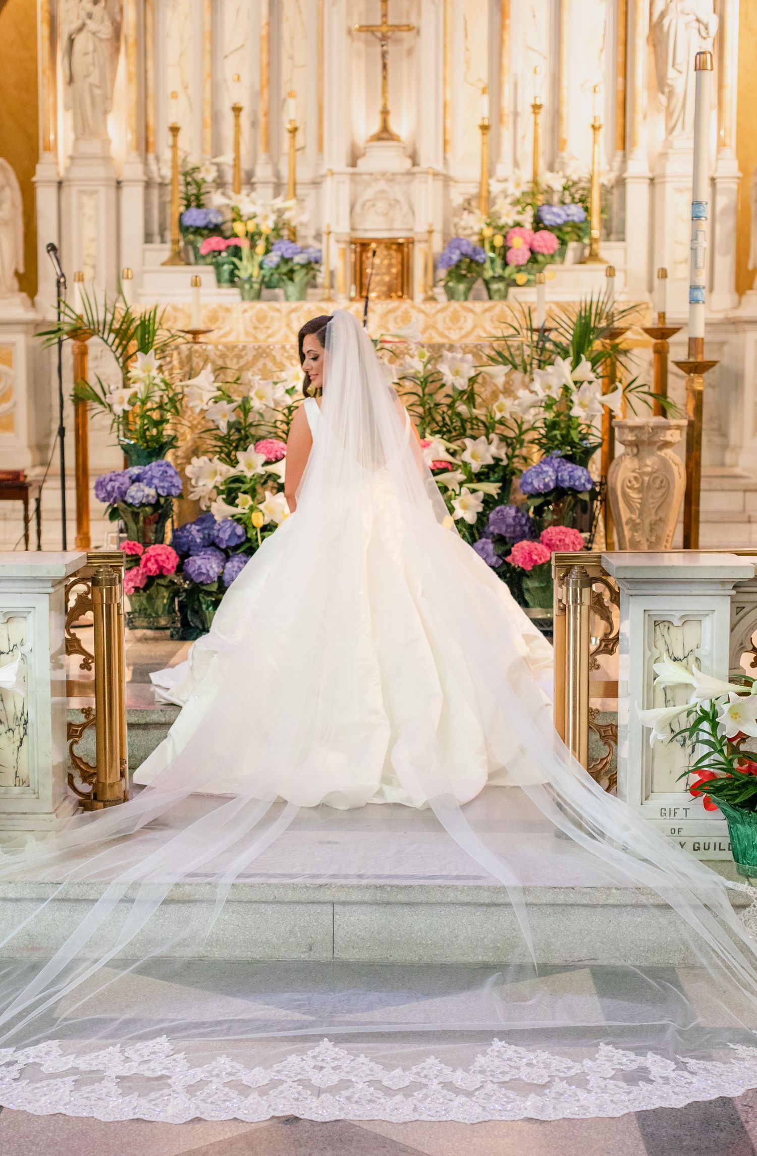 A flowing white wedding dress train with lace details spreads across a church altar floor.