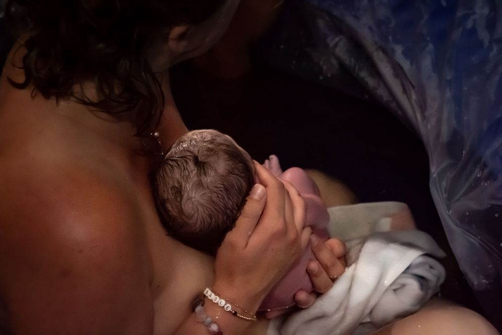 Intimate moment of skin-to-skin bonding with newborn in dim lighting.