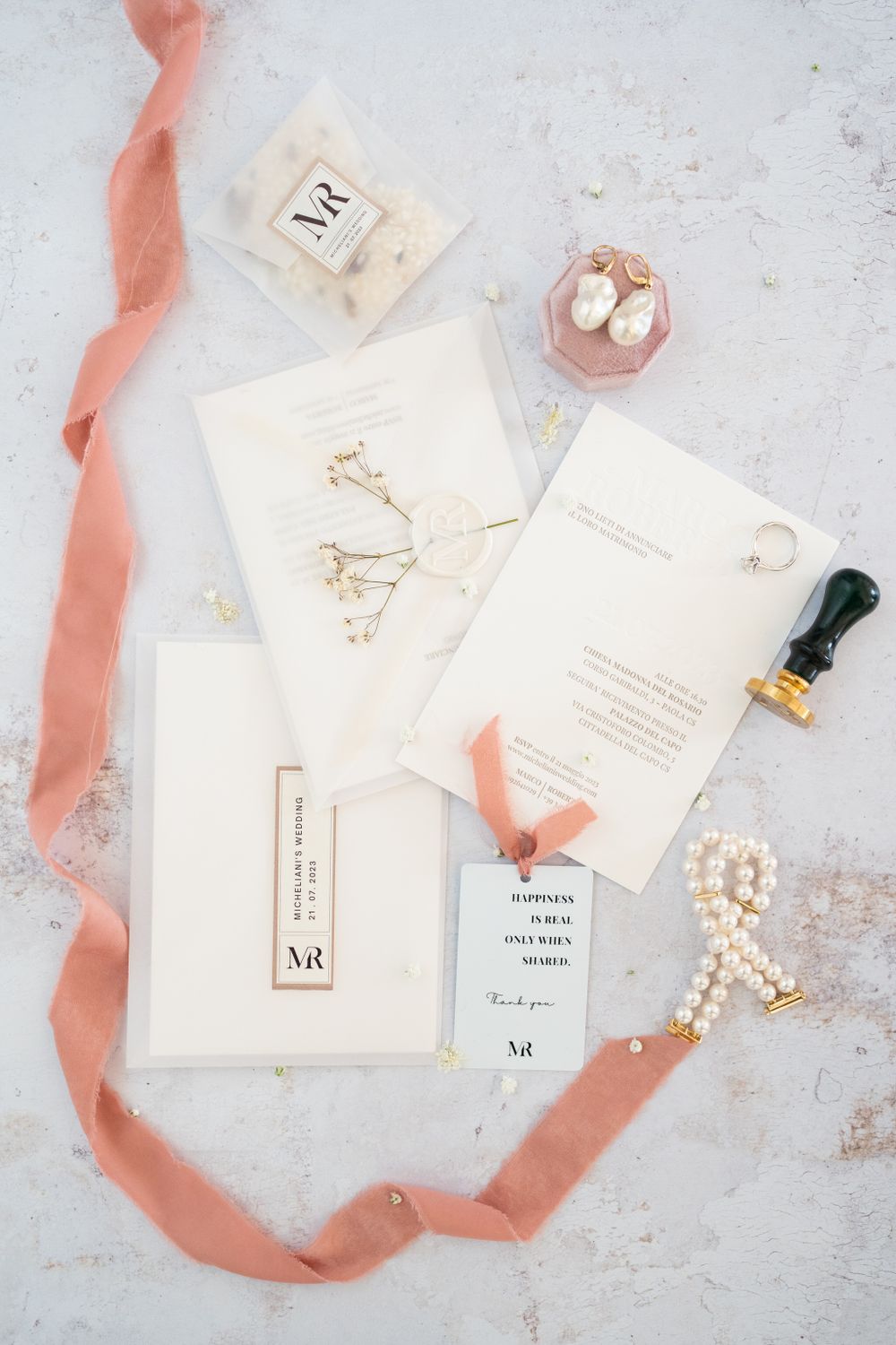 Elegant wedding stationery with white cards, pink ribbon, and pearl accents on a textured surface.