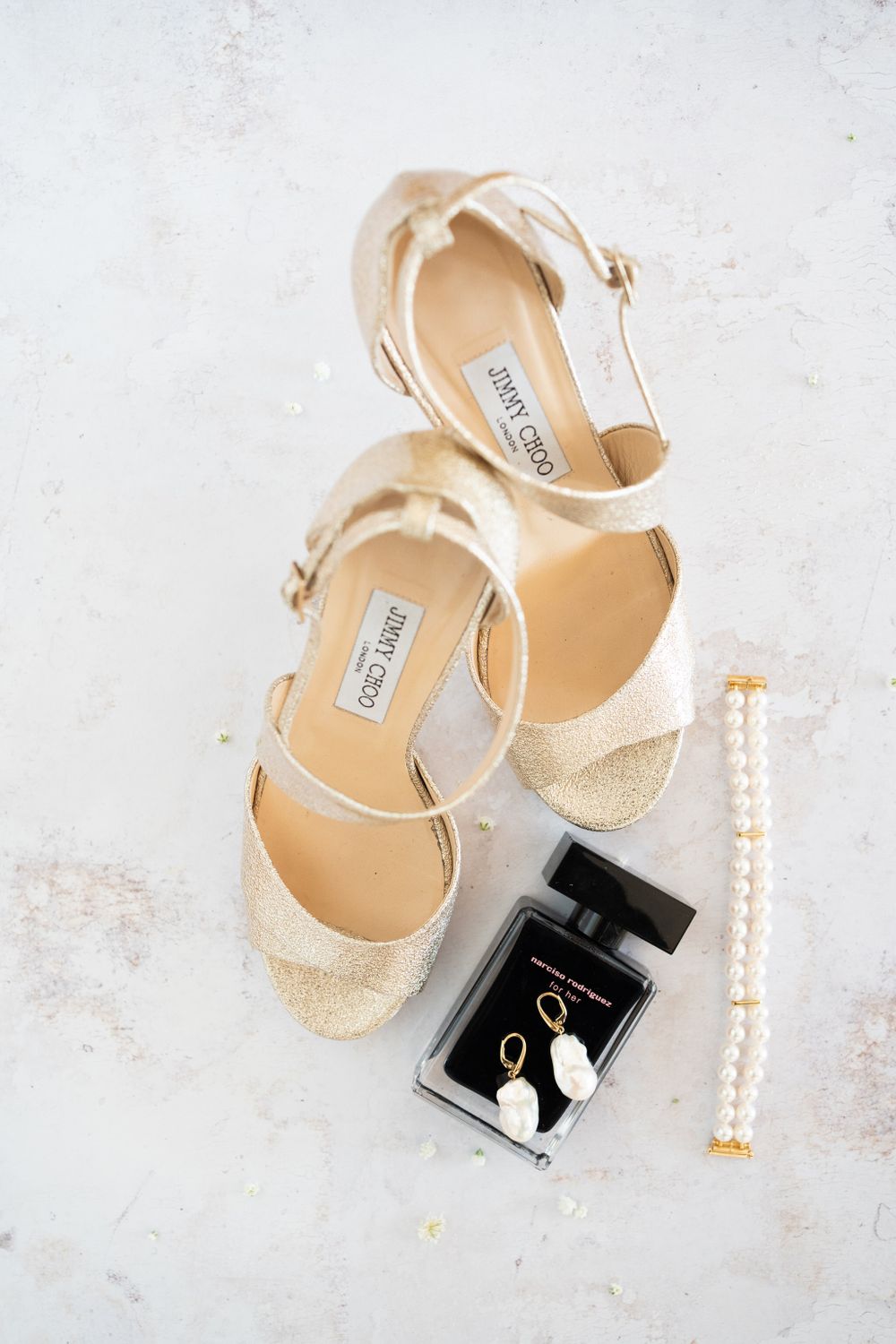 Champagne colored bridal shoes with pearl accessories and black box on marble surface.