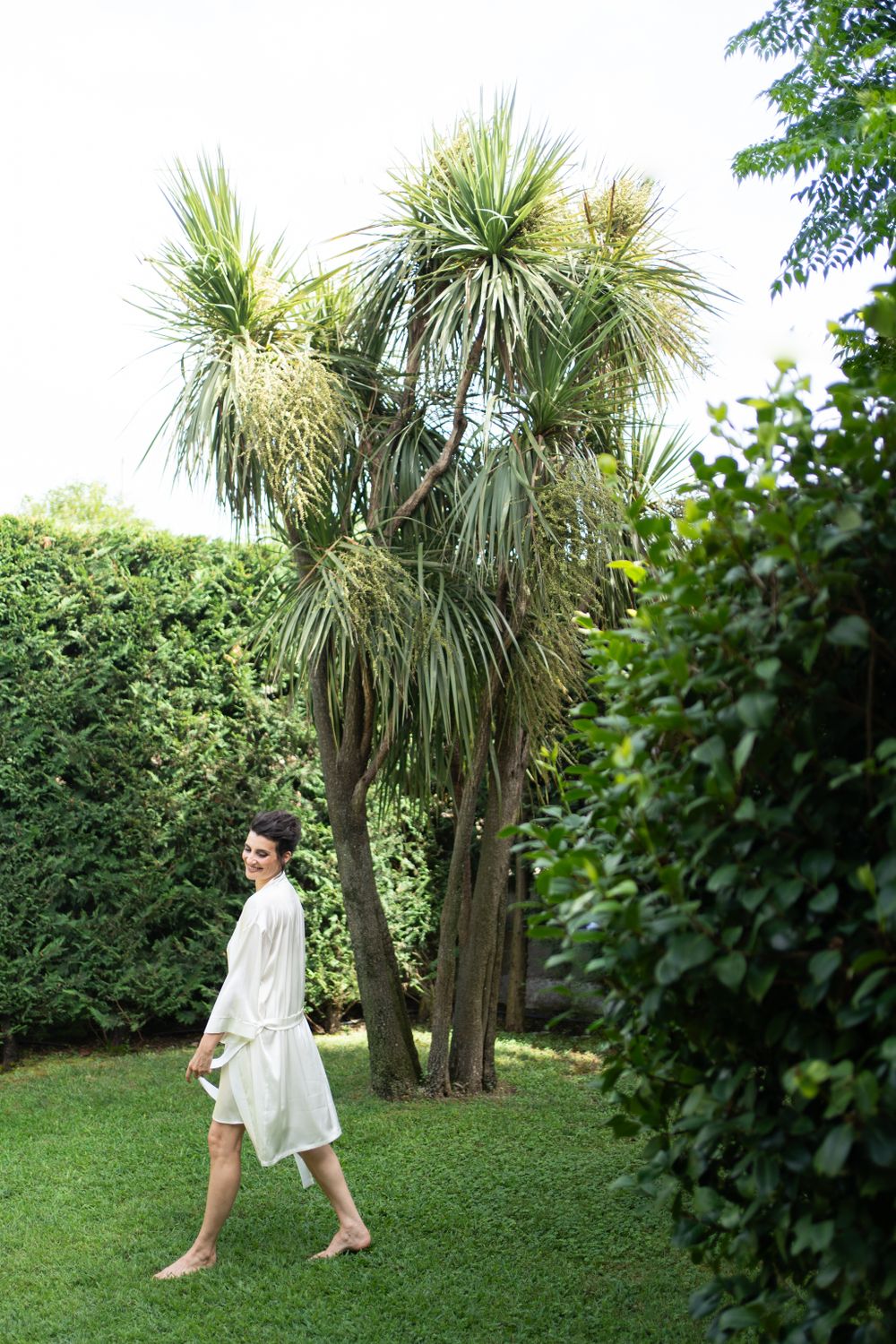 Person in white outfit walks gracefully through garden landscape with palm trees.