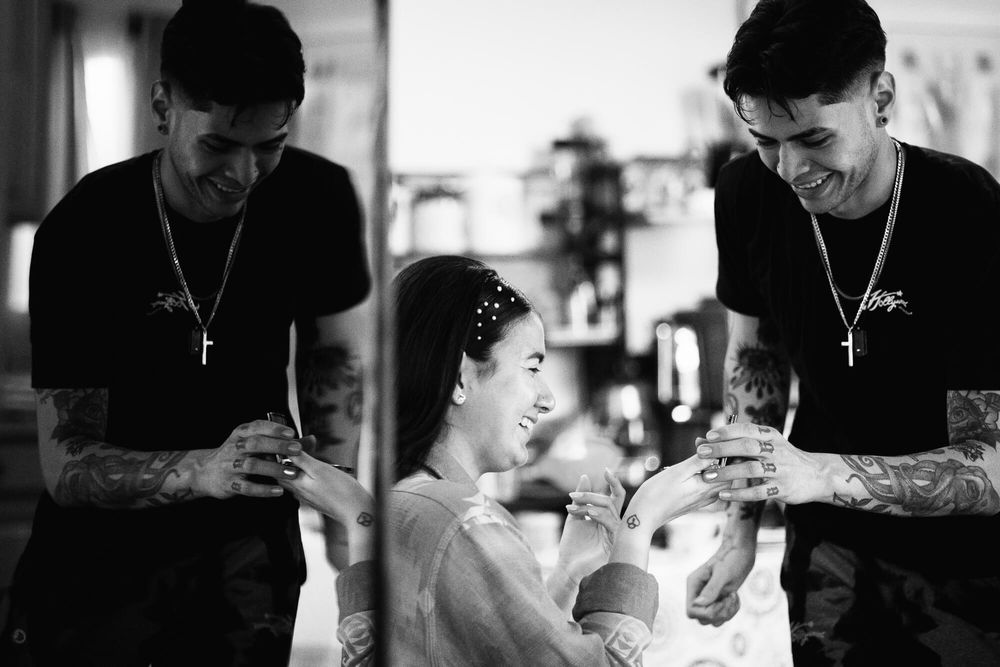A bride and her make-up artist are reflected in the screen of a large television as they laugh together getting ready.