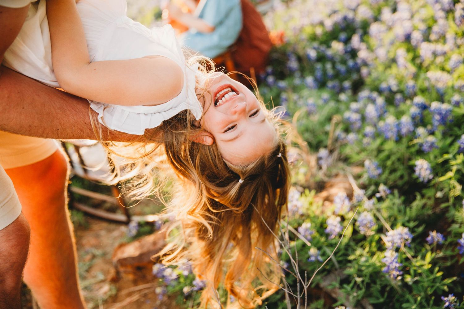 Person with flowing hair laughing joyfully in garden with purple flowers.