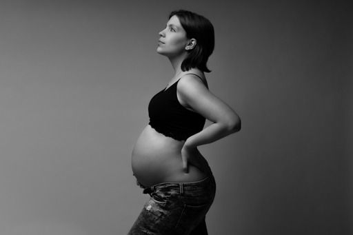 Black and white profile portrait of a pregnant woman in a crop top and jeans cradling her baby bump.