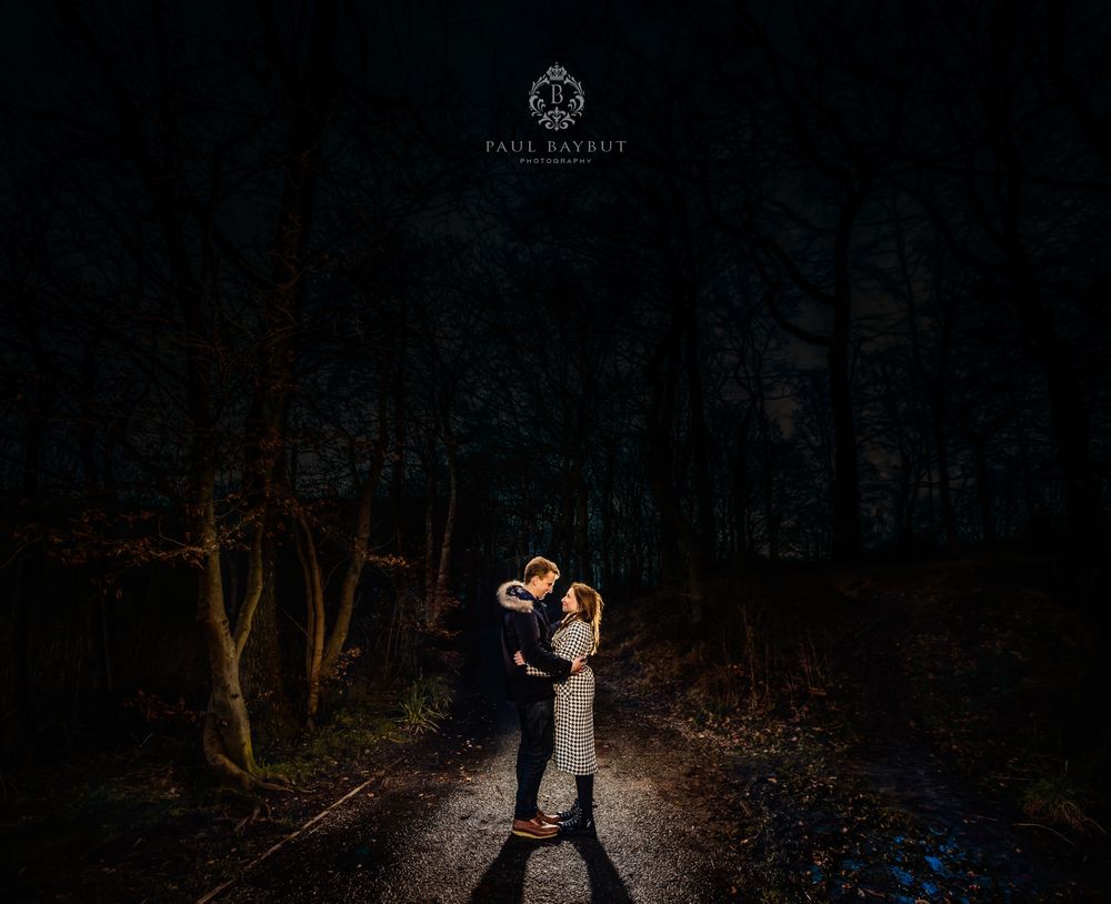 Engaged couple stand and embrace each other at night in Worsley woods Manchester during an engagement shoot