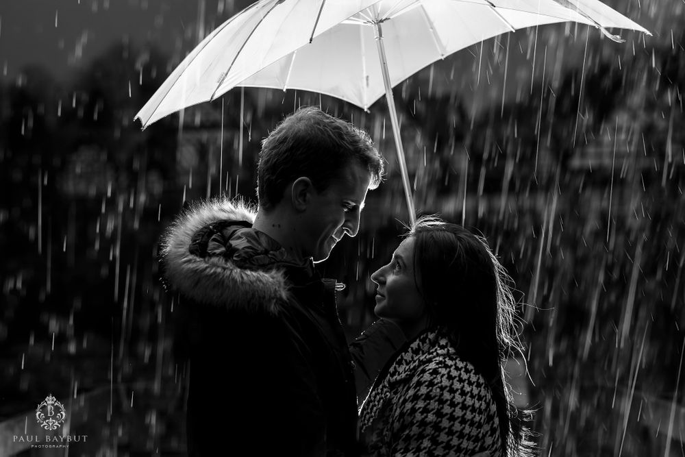 Man and woman looking into each others eyes under an umbrella in the rain on their engagement in Worsley woods
