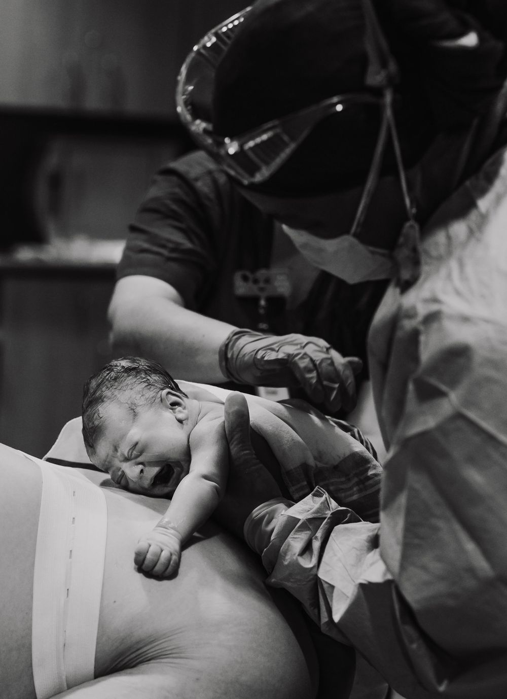 Medical professional in protective gear assists with newborn delivery.