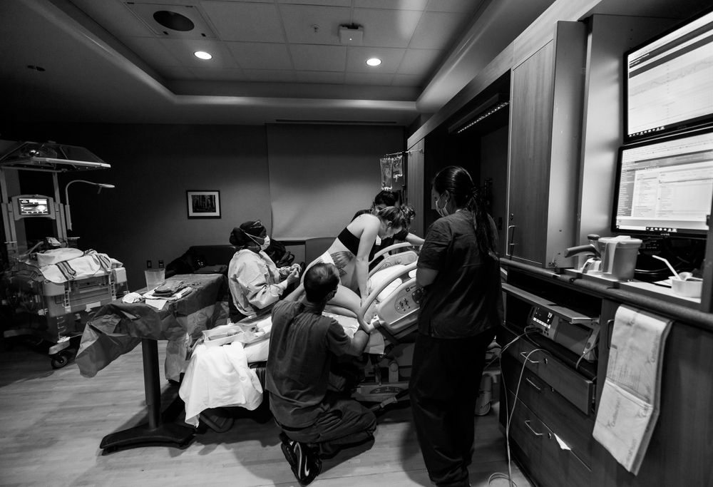 Healthcare providers assist during a delivery in a dimly lit hospital room.