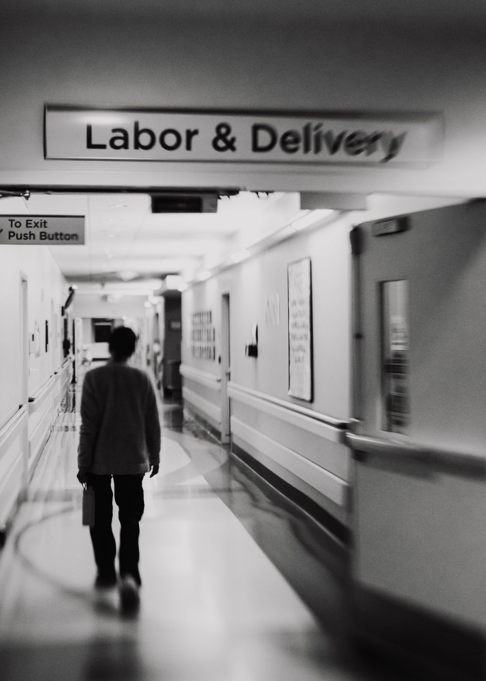 Silhouette of person walking under Labor & Delivery hospital sign in corridor.