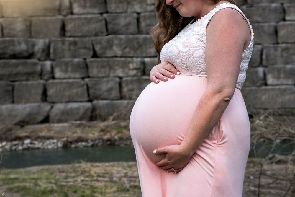 A maternity shoot at the bowmanville creek. Mom is pregnant with Twins, wearing a pink dress. Close up shot of her holding her belly.