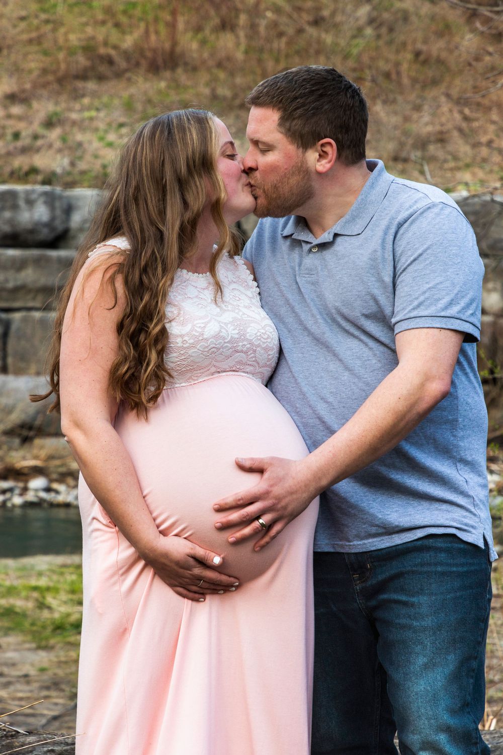 Pregnant woman and her husband kissing and holding her belly.