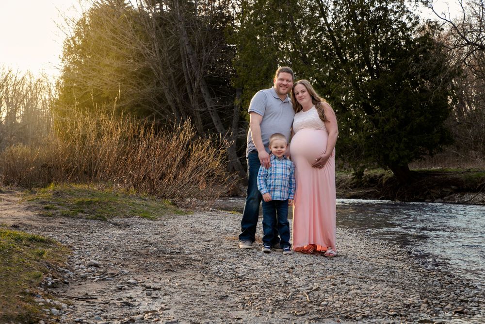 A maternity shoot. Mom is pregnant with Twins, wearing a pink dress. Family shot with their son with the creek off to the side