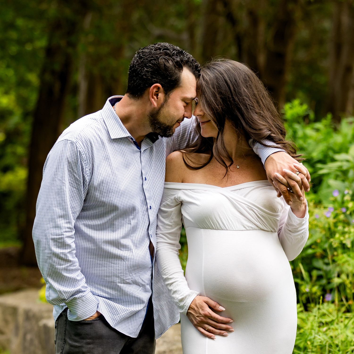 A couple shares an intimate moment in a forest setting while celebrating an expected arrival together.