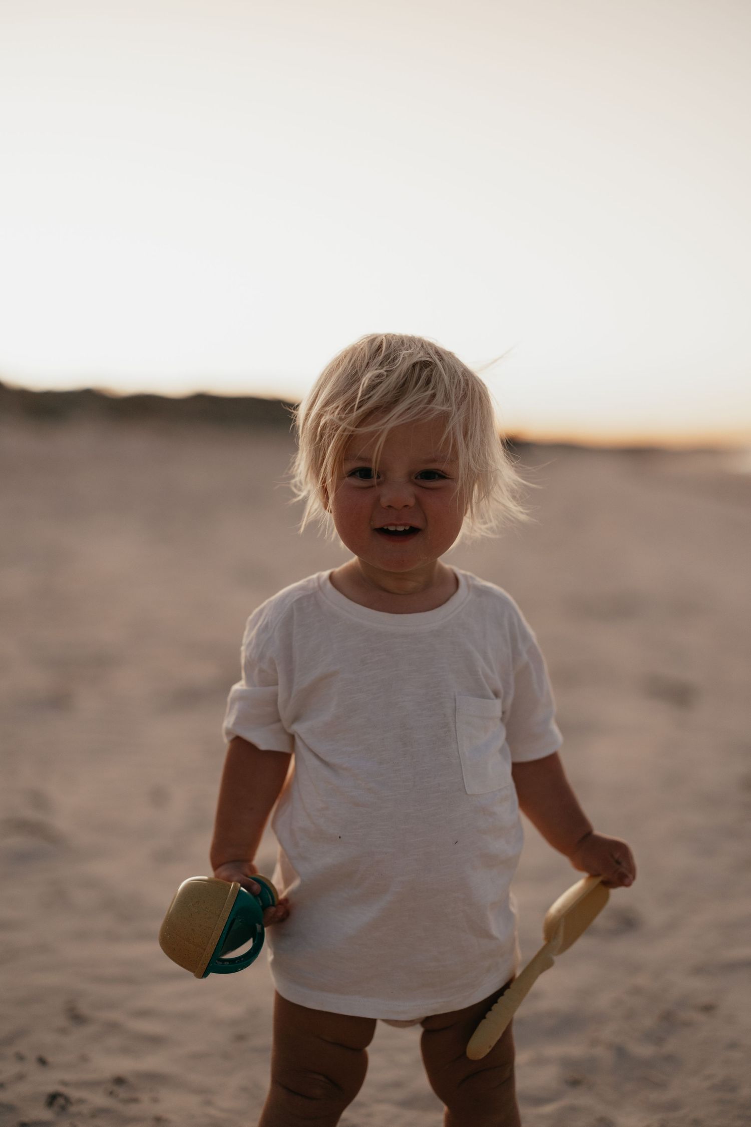 Toddler in white t-shirt playing on sandy beach at sunset.