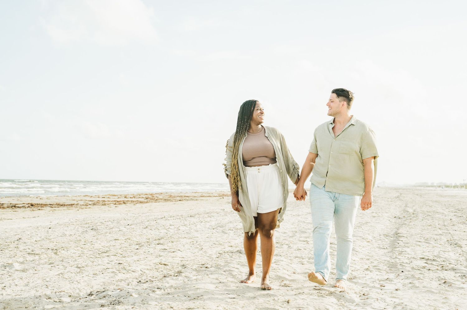 Couple strolling together on sunny beach with soft natural lighting.