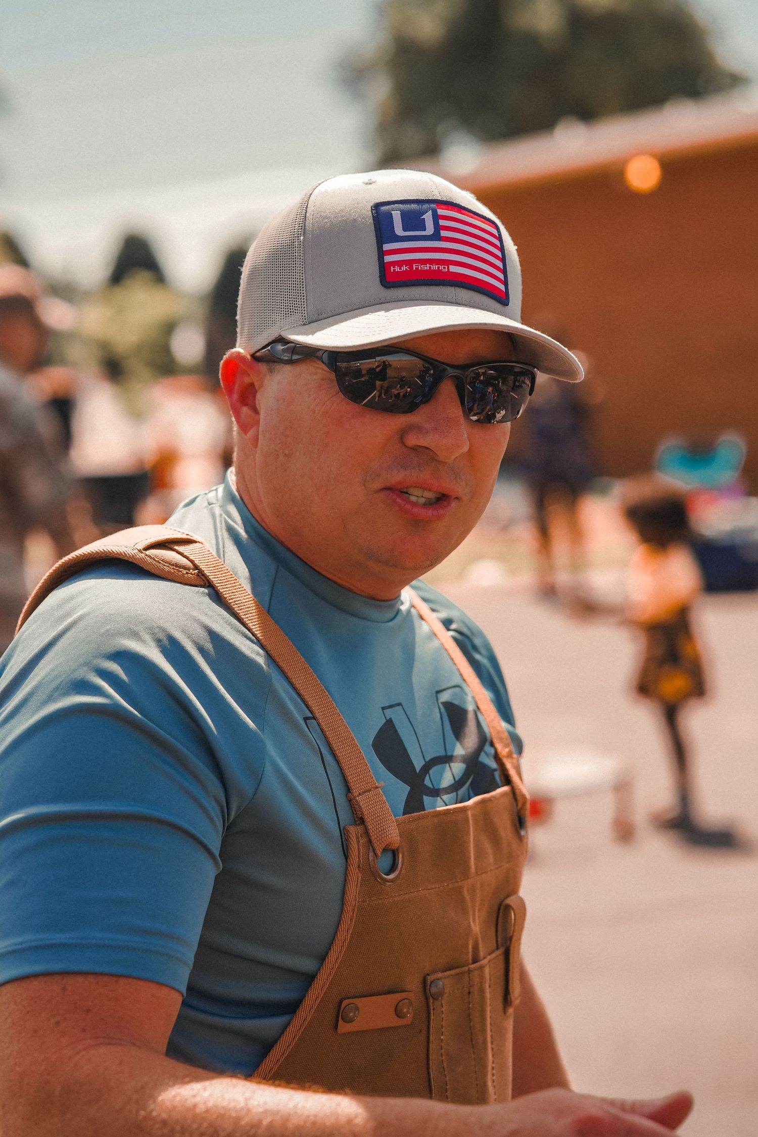 Person wearing overalls and USA flag cap at outdoor summer event.