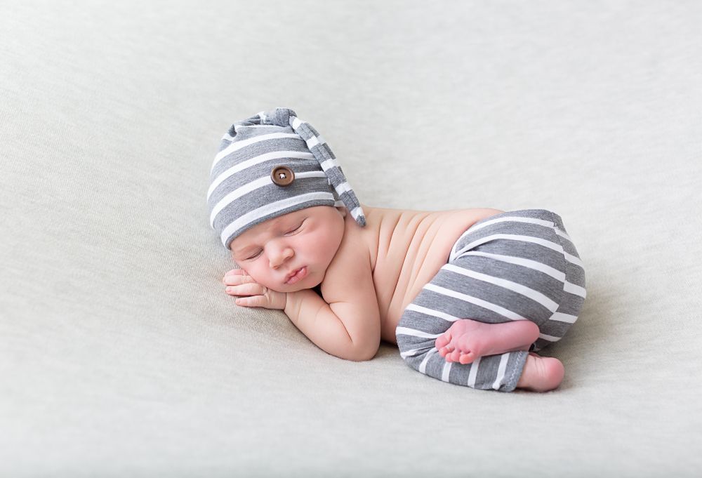 Baby wearing striped outfit lying peacefully on light gray background.