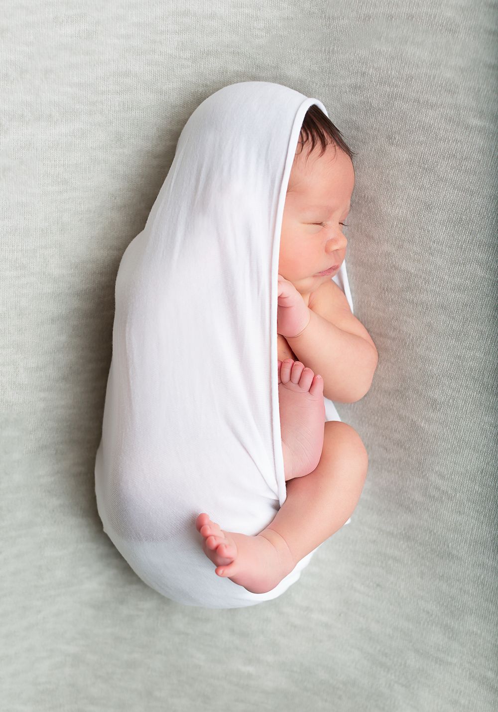 Collection of peaceful newborn poses wrapped in white fabric on gray surface.