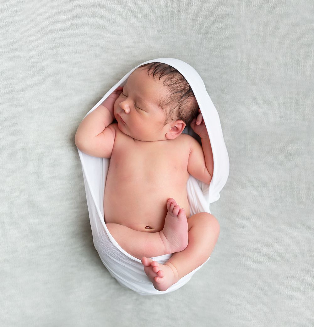 Artistic newborn photography series showing baby wrapped in white fabric.