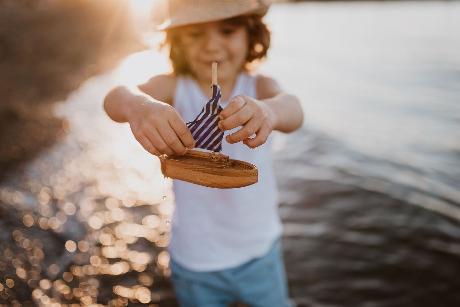 Young boy holding a toy wooden boat at sunset at Jericho Beach.