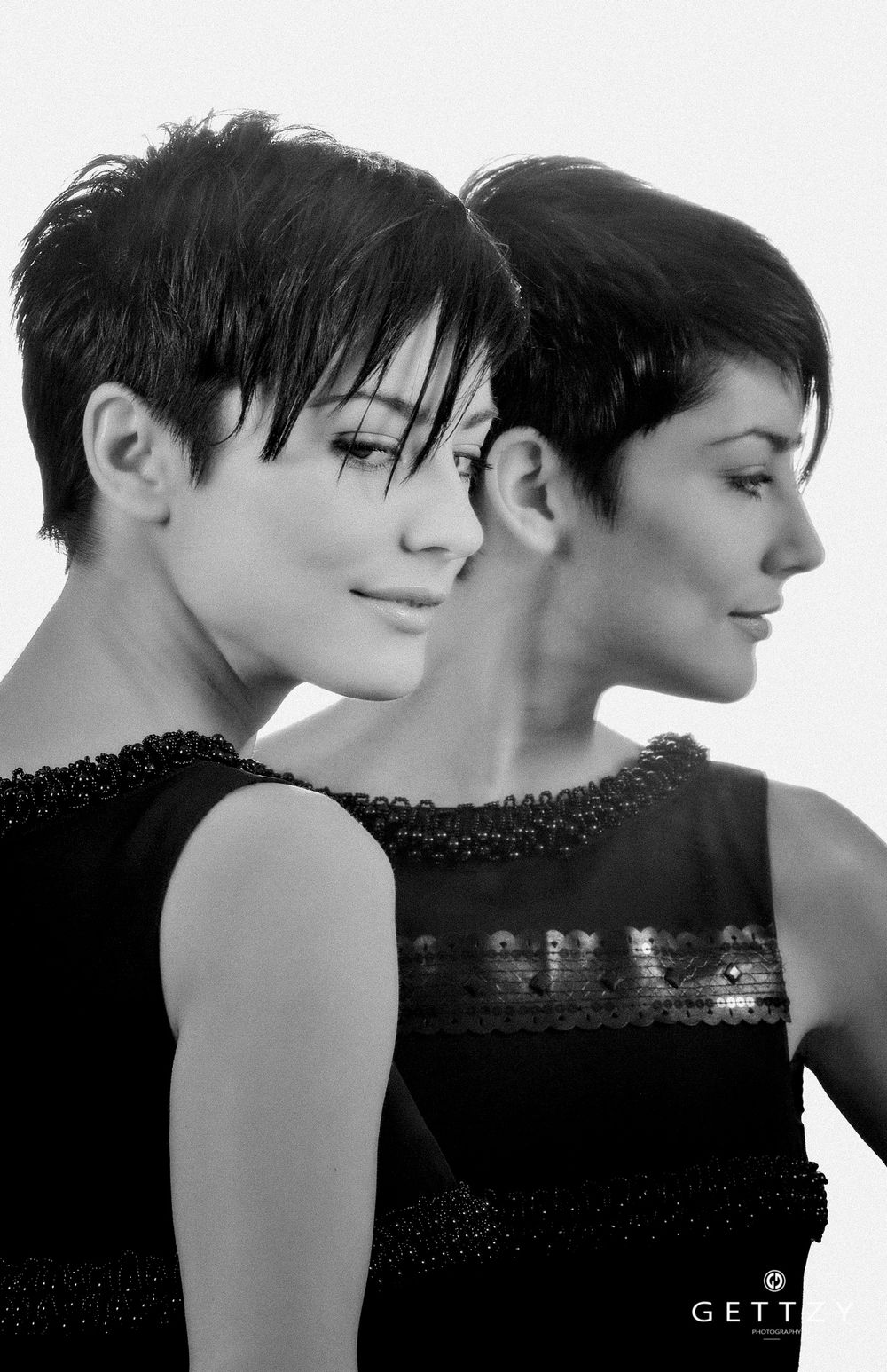 Artistic black and white portrait showing a reflection in a mirror with a short pixie haircut and elegant black dress.